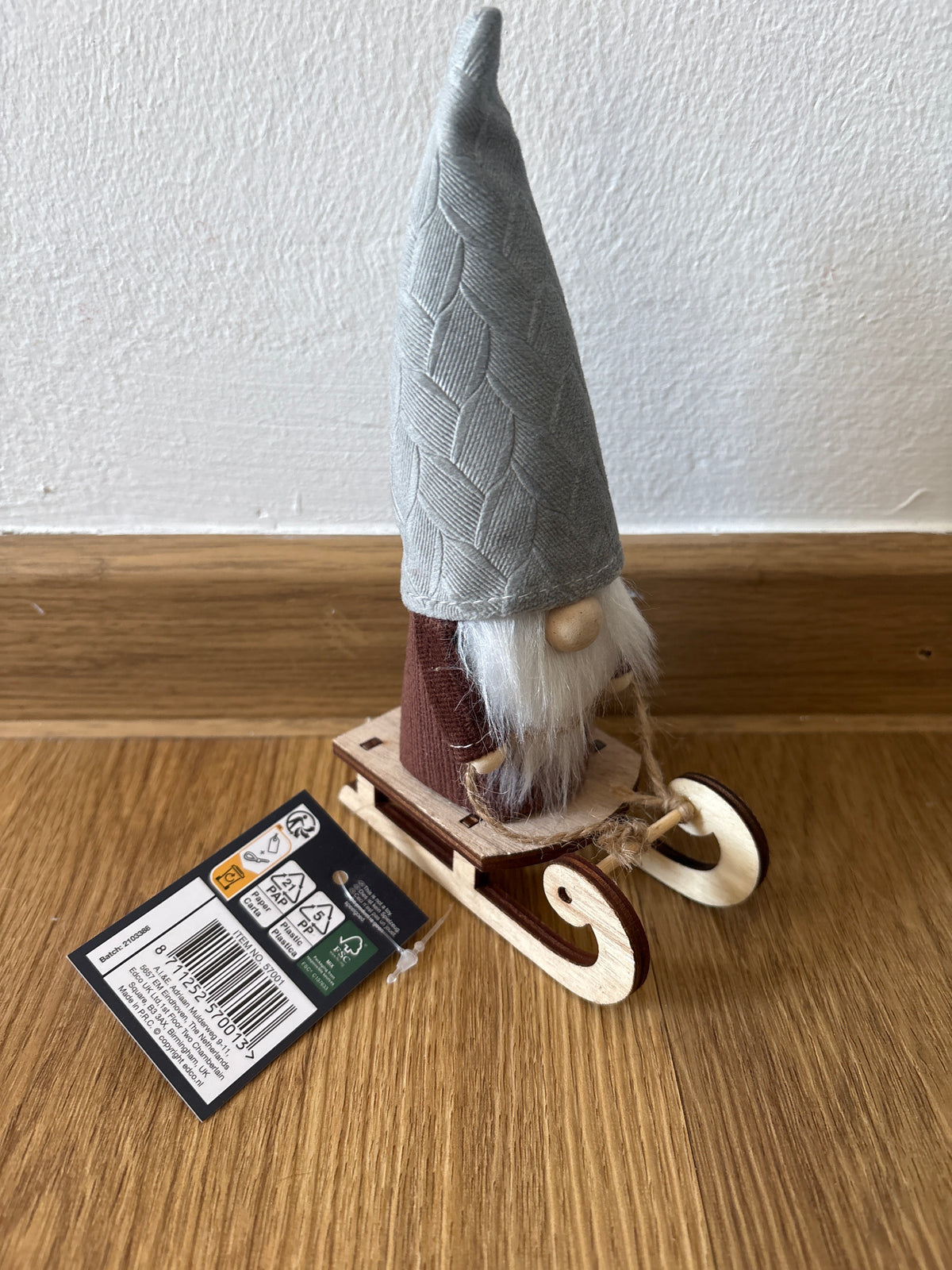 Deko kleiner Weihnachtszwerg auf einem Schlitten, graue Mütze