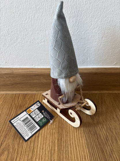 Deko kleiner Weihnachtszwerg auf einem Schlitten, graue Mütze