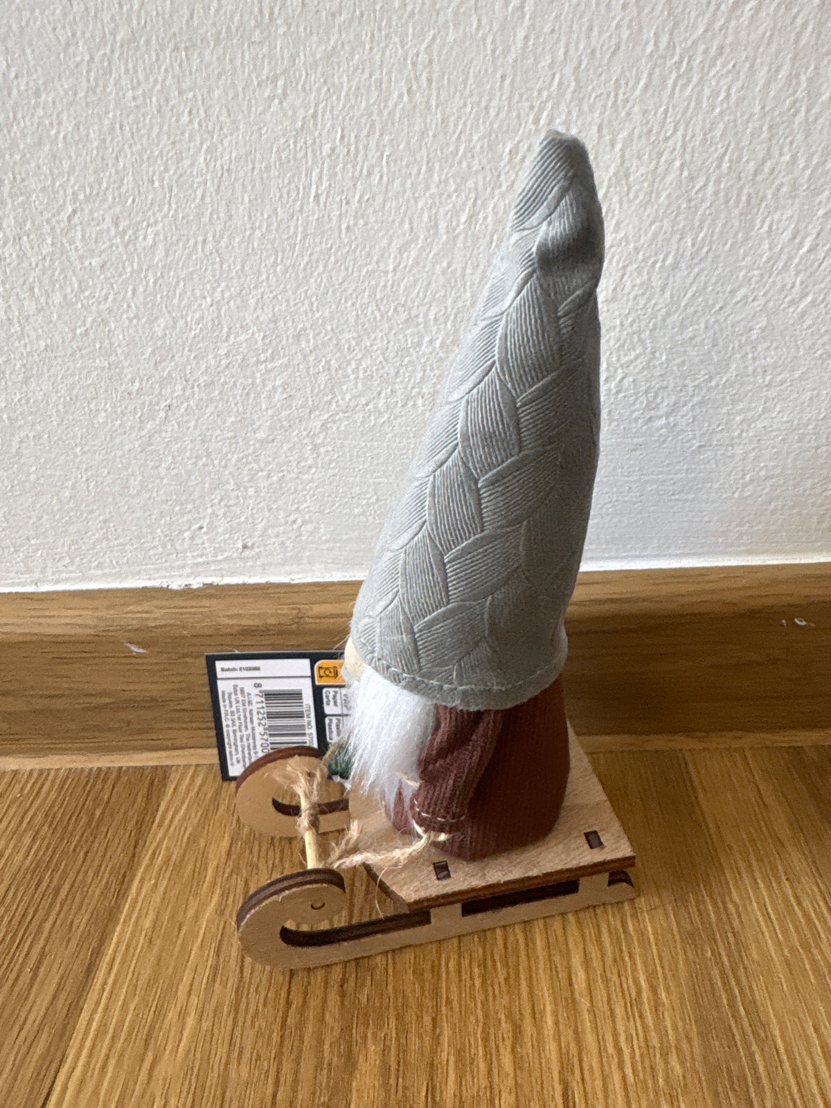 Deko kleiner Weihnachtszwerg auf einem Schlitten, graue Mütze