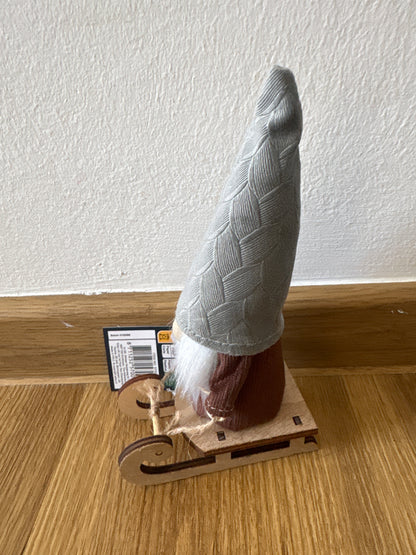Deko kleiner Weihnachtszwerg auf einem Schlitten, graue Mütze