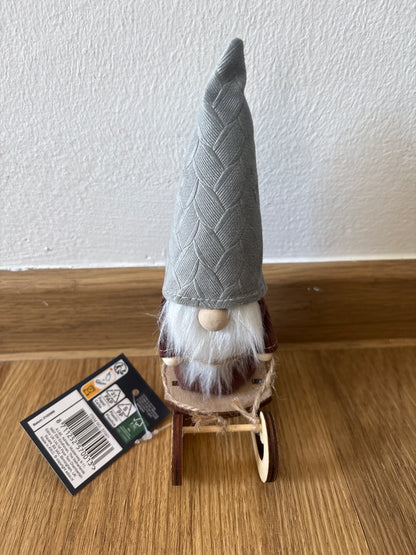 Deko kleiner Weihnachtszwerg auf einem Schlitten, graue Mütze